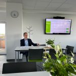 Im hellen Sitzungssaal sitzt ein Mann am Besprechungstisch, während auf dem Monitor die HEMER-Oberfläche mit Terminen und Einträgen zu sehen ist.